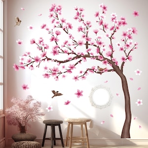 May include: A wall decal featuring a stylized cherry blossom tree with pink flowers and brown branches. The design includes falling petals and small birds, creating a spring-like atmosphere. Two wooden stools are in the foreground.