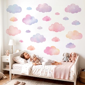May include: A set of wall decals featuring various watercolor-style clouds in shades of pink, purple, blue, and orange. The clouds are arranged in different sizes across the wall, displaying soft, blended pastel colors and rounded shapes.