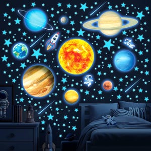 May include: A set of glow-in-the-dark wall decals featuring a large yellow sun, various planets including Saturn with rings, Earth, Jupiter, and Mars, along with a rocket ship, two astronauts, and numerous blue stars and shooting star streaks.