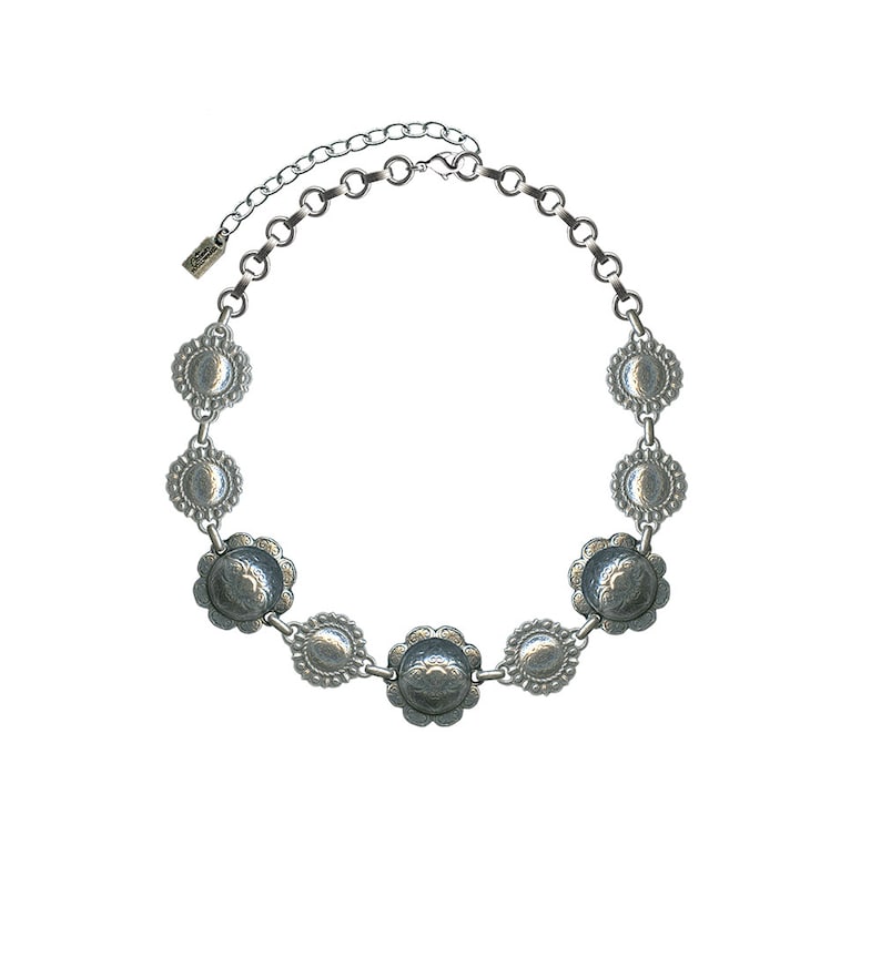 Op de afbeelding: Een zilveren ketting met een ketting en ronde, decoratieve hangers. De hangers hebben een gegolfde rand en een reli&euml;fdesign.