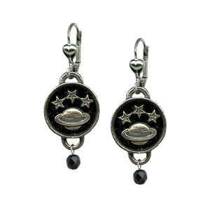 May include: Silver dangle earrings with a black enamel circle charm featuring a silver planet with rings and three stars. The charm is attached to a black bead.