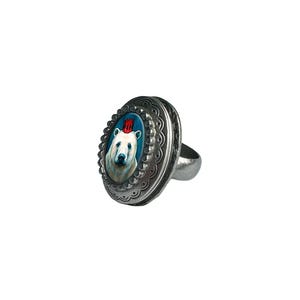 May include: A silver ring with an oval-shaped cameo featuring a white polar bear wearing a red crown. The cameo is set against a blue background.