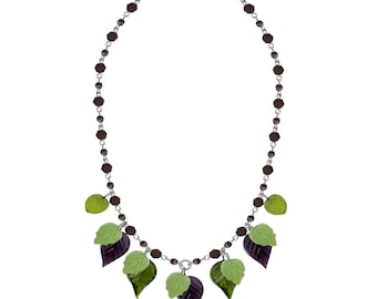 May include: A necklace with a silver chain and dark brown beads. It features leaf pendants in green and purple. The leaves are arranged symmetrically, creating a nature-inspired design. The necklace is suitable for everyday wear.