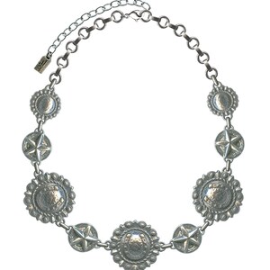 May include: Silver-toned necklace featuring a series of decorative medallions and star-shaped accents. The necklace has a chain with an adjustable length. The medallions have a detailed, textured design. The necklace is designed to be worn around the neck.