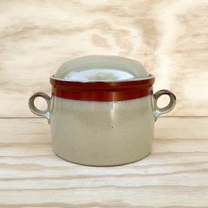 May include: A ceramic casserole dish with a lid. The dish is light gray with a speckled texture and a dark brown band around the middle. It has two small handles and a matching lid. The lid is light gray with a slightly darker rim.