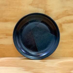 May include: A round, ceramic plate with a dark blue and teal glaze. The plate's surface features a geometric design and a glossy finish. The plate is suitable for serving food and is a decorative item for the kitchen or dining room.