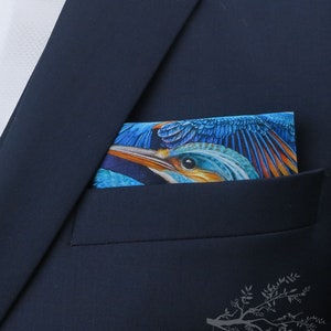 Puede incluir: Una chaqueta de traje azul marino con un pañuelo de bolsillo que presenta una ilustración de un pájaro colorido. El pañuelo de bolsillo tiene una combinación de colores azul, verde, naranja y amarillo.