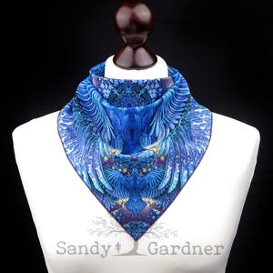 May include: A blue and purple silk scarf with a detailed design of a bird with outstretched wings. The scarf is displayed on a white mannequin bust.