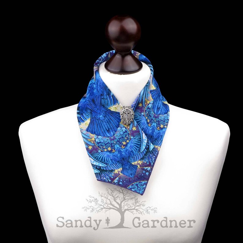 May include: A blue and gold patterned neck scarf with a silver pin. The scarf is on a white mannequin bust.