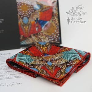 May include: A red silk pocket square with a colorful pheasant print. The square is folded and has a fringed edge. The text "Sandy Gardner" is visible in the background.