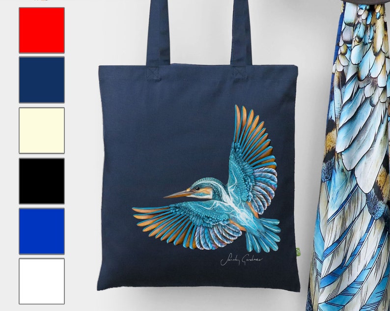 K&ouml;nnte beinhalten: Eine marineblaue Tragetasche mit einer farbenfrohen Illustration eines Eisvogels im Flug. Die Tasche hat ein gr&uuml;nes Etikett mit dem Text "Sindy Cobber" in Wei&szlig;.
