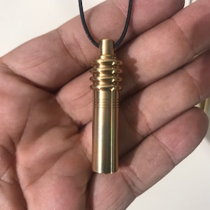 May include: A gold-colored pendant with a cylindrical design and a black cord. The pendant has a series of ribbed sections and a smooth, polished finish. The top of the pendant has a small, cylindrical cap.