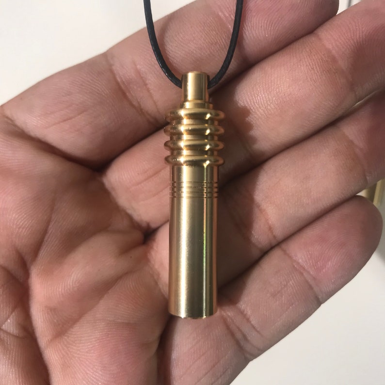 May include: A gold-colored pendant with a cylindrical design and a black cord. The pendant has a series of ribbed sections and a smooth, polished finish. The top of the pendant has a small, cylindrical cap.