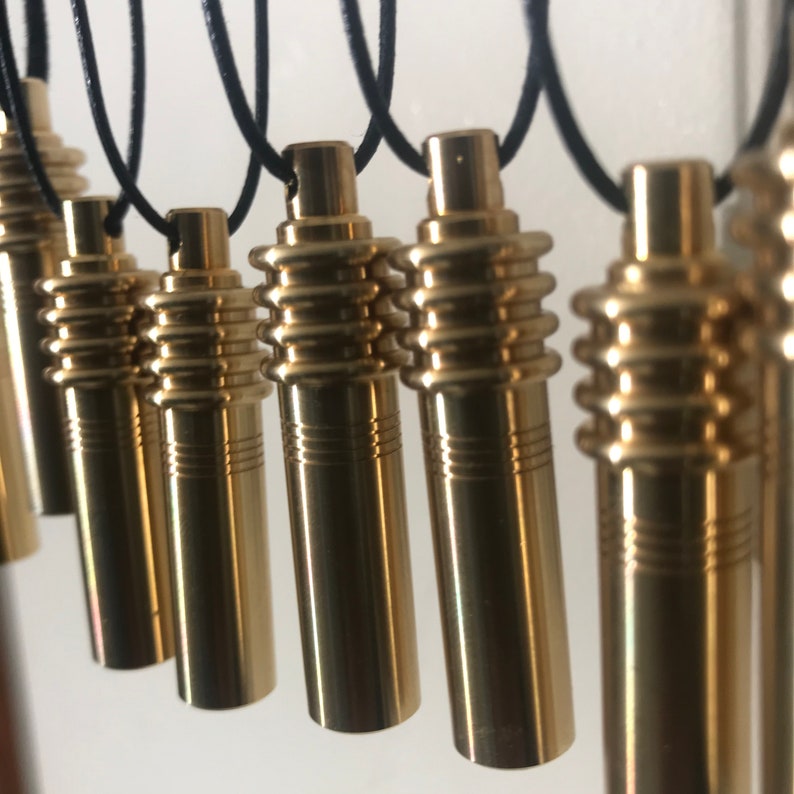 May include: A collection of gold-colored cylindrical pendants hanging from black cords. Each pendant has a ridged midsection and a smooth, rounded top. The pendants are evenly spaced and appear to be made of metal.