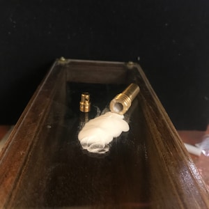 May include: Two small, brass-colored metal components and a larger brass-colored metal component with a white substance inside. The items are on a dark, reflective surface.