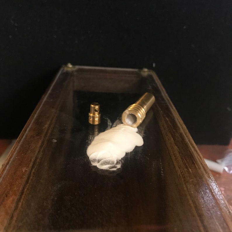 May include: Two small, brass-colored metal components and a larger brass-colored metal component with a white substance inside. The items are on a dark, reflective surface.
