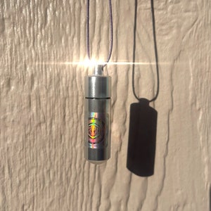 May include: A silver necklace with a small, cylindrical pendant. The pendant has a holographic sticker with a geometric design.