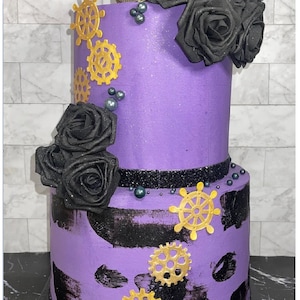 May include: A two-tiered purple cake decorated with black roses, gold gears, and black and gold accents. The cake is on a white tiled surface.