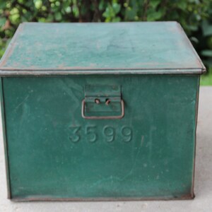May include: A vintage green metal box with a hinged lid and a handle. The box has the number "3599" embossed on the front. The box is rectangular and appears to be made of metal. The box is likely used for storage.