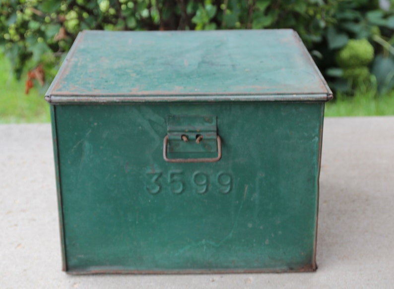 May include: A vintage green metal box with a hinged lid and a handle. The box has the number "3599" embossed on the front. The box is rectangular and appears to be made of metal. The box is likely used for storage.
