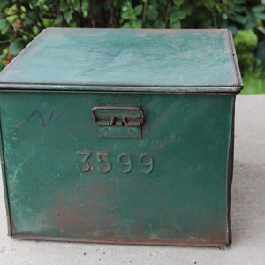 May include: A vintage, rectangular, green metal box with a hinged lid and a metal handle. The box has the number "3599" embossed on the front. The paint is distressed, showing signs of age and wear.