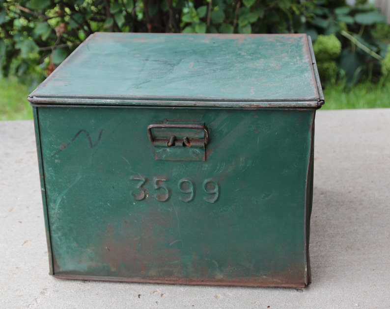 May include: A vintage, rectangular, green metal box with a hinged lid and a metal handle. The box has the number "3599" embossed on the front. The paint is distressed, showing signs of age and wear.
