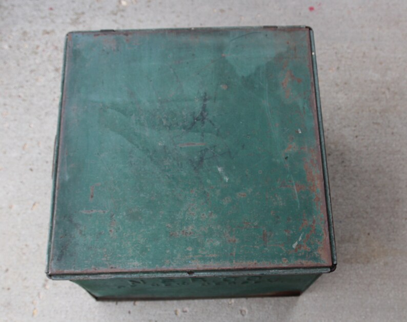 May include: A vintage, square metal box with a hinged lid. The box is painted a distressed green color with visible rust spots, giving it a rustic appearance. The box is likely used for storage.