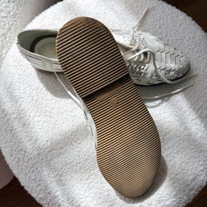May include: White woven leather shoes with a brown rubber sole. The shoes have white laces and are displayed on a white, textured surface. The sole has a grooved pattern for traction. The shoes appear to be new.