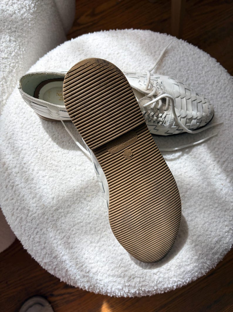 May include: White woven leather shoes with a brown rubber sole. The shoes have white laces and are displayed on a white, textured surface. The sole has a grooved pattern for traction. The shoes appear to be new.