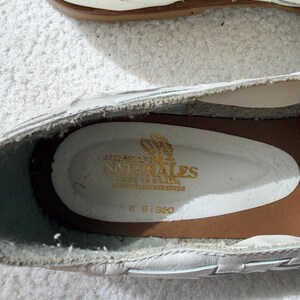 May include: White leather shoes with a woven design. The interior shows the brand name "NATURALES" in gold lettering, along with "MADE IN BRAZIL" and "GENUINE LEATHER UPPER". The shoes have a brown sole.