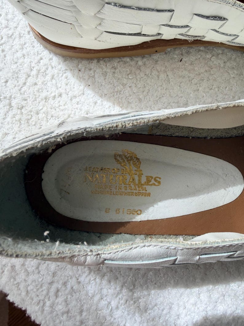 May include: White leather shoes with a woven design. The interior shows the brand name "NATURALES" in gold lettering, along with "MADE IN BRAZIL" and "GENUINE LEATHER UPPER". The shoes have a brown sole.