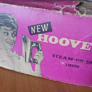 May include: A pink box with the text "NEW HOOVER STEAM-OR-DRY IRON" on it. A woman is holding a white iron with a black handle.