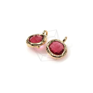 Puede incluir: Dos abalorios de metal dorado con piedras de cristal rojo. Los abalorios tienen un diseño texturizado y adornado alrededor de las piedras.