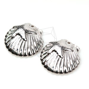 Op de afbeelding: Twee zilverkleurige metalen bedels in de vorm van schelpen met een stervormig ontwerp aan de bovenkant.