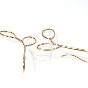 May include: A pair of gold-toned earrings with a unique, abstract design. Each earring features a curved, open loop with a smaller loop attached to it. The earrings have a simple, minimalist style.