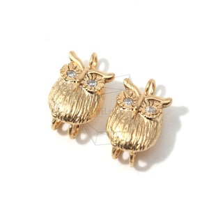 May include: Two gold owl charms with clear rhinestone eyes. The owls have a textured surface and are attached to a loop for hanging.
