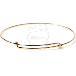 Könnte beinhalten: Ein goldfarbenes Armreif-Armband mit einem schlichten, eleganten Design. Das Armband besteht aus einem einzigen, durchgehenden Draht, der zu einem Kreis gebogen und dann an den Enden mit einem kleinen, sicheren Verschluss verbunden wird.