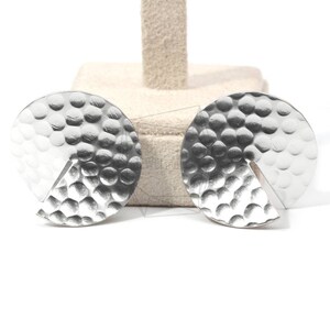 May include: A pair of silver earrings with a textured, circular design. Each earring has a cut-out section, creating a unique geometric shape.