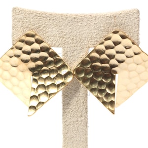 May include: A pair of gold-tone earrings with a hammered texture. The earrings are shaped like a teardrop with a pointed tip.