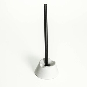 May include: A white concrete pen holder with a black pen standing upright in it.