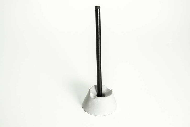 May include: A white concrete pen holder with a black pen standing upright in it.