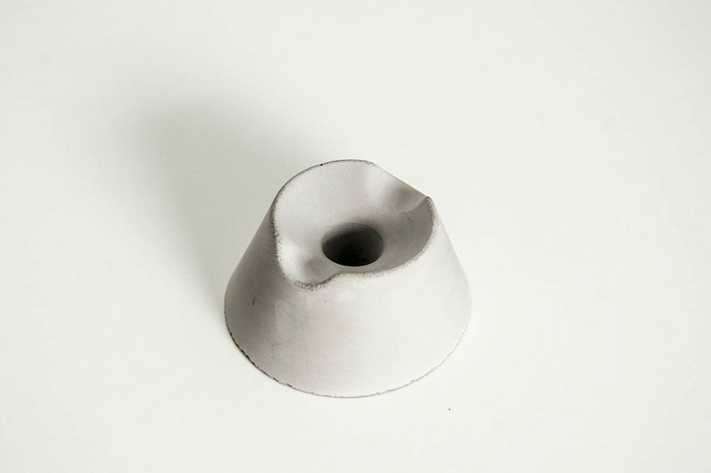 May include: A white concrete pen holder with a rounded, organic shape and a hole in the center for holding pens or pencils.