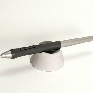 May include: A black and silver stylus pen resting on a gray ceramic stand.