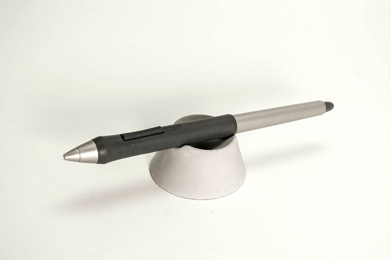 May include: A black and silver stylus pen resting on a gray ceramic stand.
