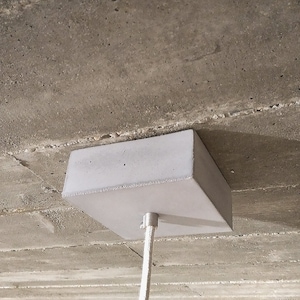 May include: A white concrete ceiling light fitting with a square base and a white cord.