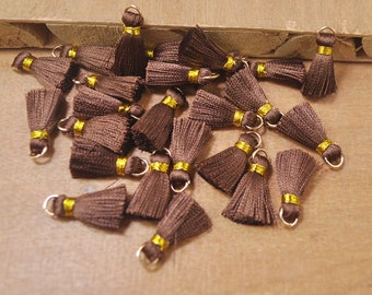May include: A group of brown silk tassels with gold trim and a gold loop at the top. The tassels are scattered on a wooden surface.