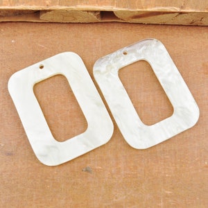 Può includere: Due forme rettangolari in plastica bianca con un foro in alto e un foro rettangolare più piccolo al centro.