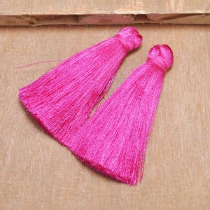 May include: Two bright pink silk tassels with a knotted top. The tassels are made of soft, fine threads and are perfect for adding a touch of color and texture to any project.