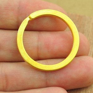 Puede incluir: Primer plano de un llavero de color dorado. El llavero es circular y está hecho de metal. El llavero está en la mano de una persona.