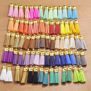 Puede incluir: Surtido de 50 borlas de gamuza de colores vivos con tapas de metal dorado. Las borlas están dispuestas en filas por color, con 5 borlas en cada fila.